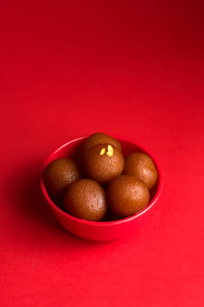 Gulab Jamun in red bowl on red background. Indian Dessert or Sweet Dish.