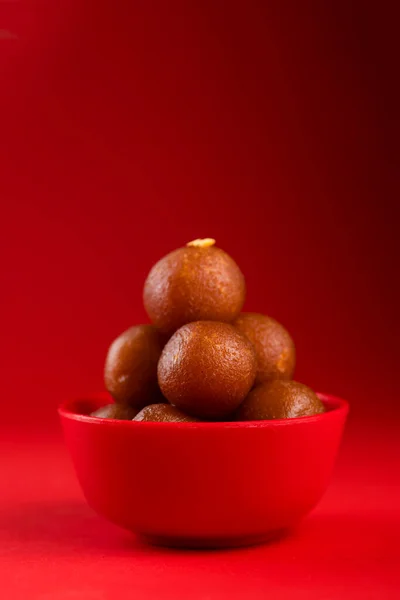 Gulab Jamun in red bowl on red background. Indian Dessert or Sweet Dish.