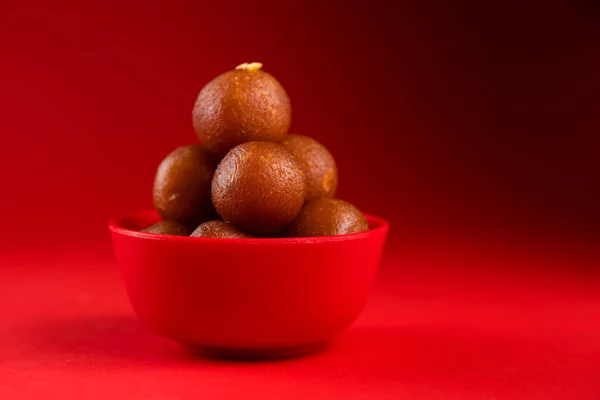 Gulab Jamun in red bowl on red background. Indian Dessert or Sweet Dish.