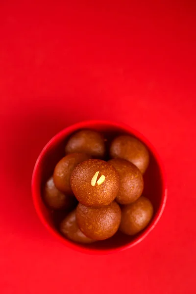 Gulab Jamun in red bowl on red background. Indian Dessert or Sweet Dish.