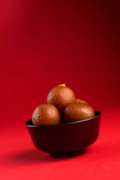 Gulab Jamun v černé míse na červeném pozadí. Indický dezert nebo sladké jídlo. — Stock fotografie