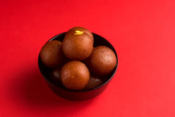 빨간 배경검은 접시에 검은 색 바가지를 두르고 있습니다. 인도식 디저트나 달콤 한 음식. — 스톡 사진