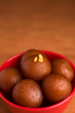 Ahşap arka planda kırmızı kasede Gulab Jamun. Hint Tatlısı ya da Tatlı Tabak.