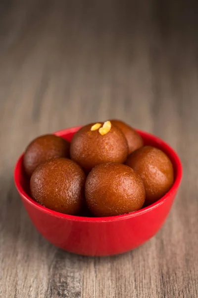 Gulab Jamun in red bowl on wooden background. Indian Dessert or Sweet Dish.
