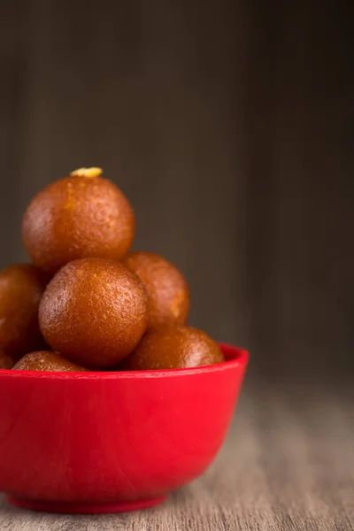 Gulab Jamun in red bowl on wooden background. Indian Dessert or Sweet Dish.