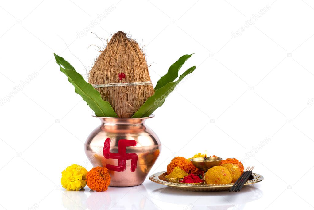 Copper Kalash with coconut and mango leaf and pooja thali with diya, kumkum and sweets with floral decoration on a white background. Essential in hindu puja.