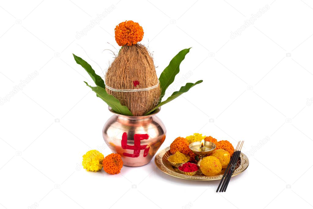 Copper Kalash with coconut and mango leaf and pooja thali with diya, kumkum and sweets with floral decoration on a white background. Essential in hindu puja.