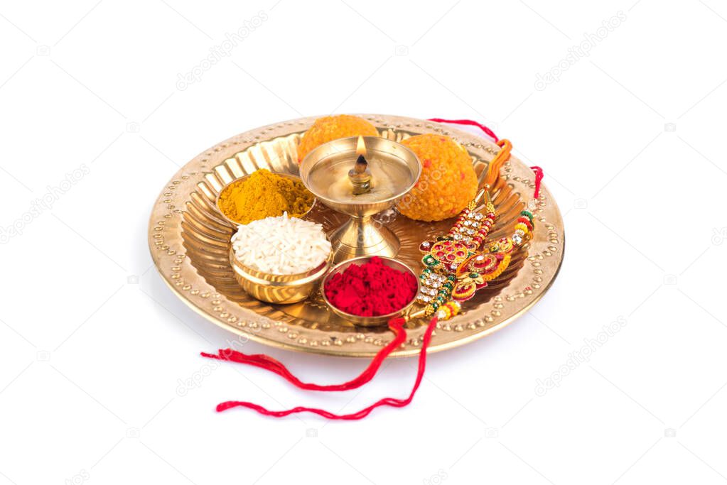 Indian Festival: Rakhi with rice grains, kumkum, sweets and diya on plate with an elegant Rakhi. A traditional Indian wrist band which is a symbol of love between Brothers and Sisters