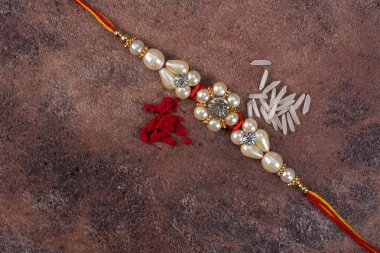 Raksha Bandhan: Taş zemin üzerinde pirinç taneleri ve kumkum bulunan Rakhi, Kardeşler ve Kardeşler arasındaki aşkın sembolü olan geleneksel Hint bilekliği.