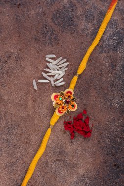 Raksha Bandhan: Taş zemin üzerinde pirinç taneleri ve kumkum bulunan Rakhi, Kardeşler ve Kardeşler arasındaki aşkın sembolü olan geleneksel Hint bilekliği.