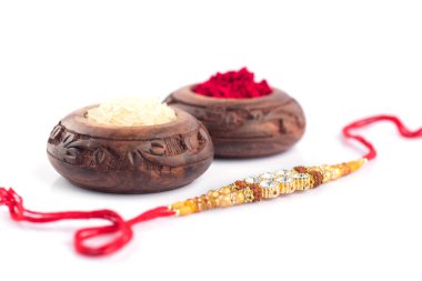 Raksha Bandhan 'ın arka planında zarif bir Rakhi, pirinç taneleri ve beyaz bir arka planda Kumkum var. Geleneksel Hint bilekliği Kardeşler ve Kız Kardeşler arasındaki aşkın sembolüdür..