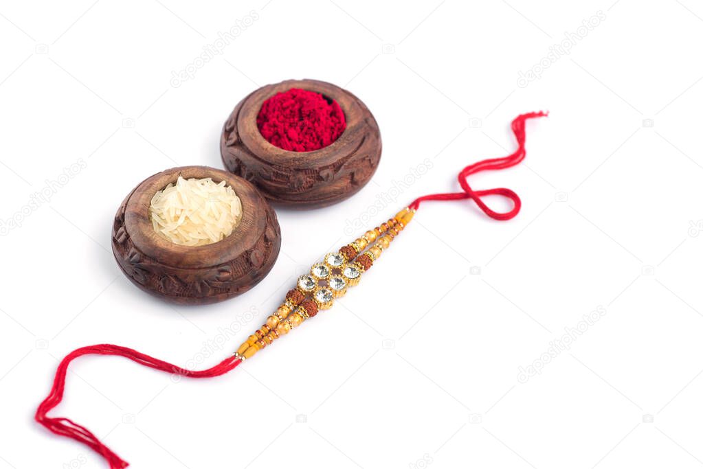 Raksha Bandhan background with an elegant Rakhi, Rice Grains and Kumkum on a white background. A traditional Indian wrist band which is a symbol of love between Brothers and Sisters.