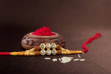 Raksha Bandhan 'ın arkaplanı zarif bir Rakhi, pirinç taneleri ve Kumkum. Geleneksel Hint bilekliği Kardeşler ve Kız Kardeşler arasındaki aşkın sembolüdür..