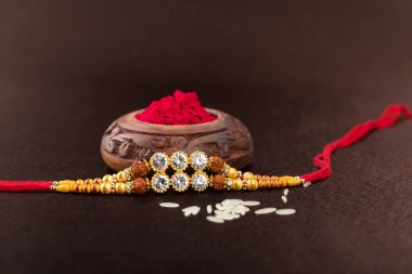 Raksha Bandhan 'ın arkaplanı zarif bir Rakhi, pirinç taneleri ve Kumkum. Geleneksel Hint bilekliği Kardeşler ve Kız Kardeşler arasındaki aşkın sembolüdür..