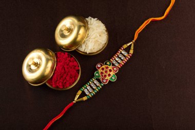 Raksha Bandhan 'ın arkaplanı zarif bir Rakhi, pirinç taneleri ve Kumkum. Geleneksel Hint bilekliği Kardeşler ve Kız Kardeşler arasındaki aşkın sembolüdür..
