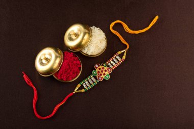 Raksha Bandhan 'ın arkaplanı zarif bir Rakhi, pirinç taneleri ve Kumkum. Geleneksel Hint bilekliği Kardeşler ve Kız Kardeşler arasındaki aşkın sembolüdür..