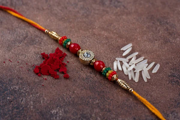 ラクシャバンダン:石の背景に米粒とクムクのラキ、兄弟姉妹の愛の象徴である伝統的なインドの手首バンド. — ストック写真