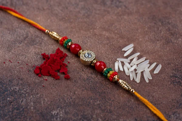 Raksha Bandhan: Rakhi med ris korn och kumkum på sten bakgrund, Traditionell indisk handled band som är en symbol för kärlek mellan bröder och systrar. — Stockfoto