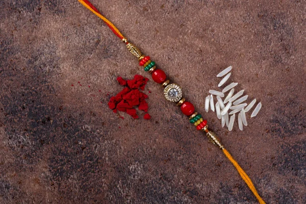 Raksha Bandhan : Rakhi with rice grains and kumkum on stone background, Traditional Indian wrist band which is a symbol of love between Brothers and Sisters. — Stock Photo, Image