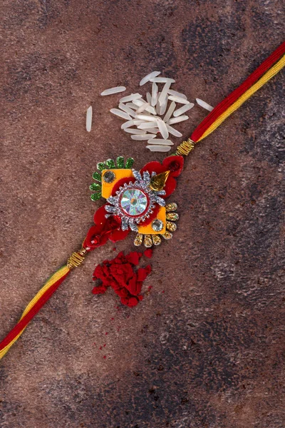 Raksha Bandhan: Taş zemin üzerinde pirinç taneleri ve kumkum bulunan Rakhi, Kardeşler ve Kardeşler arasındaki aşkın sembolü olan geleneksel Hint bilekliği. — Stok fotoğraf