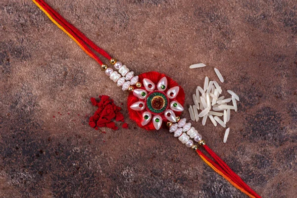 Raksha Bandhan: Taş zemin üzerinde pirinç taneleri ve kumkum bulunan Rakhi, Kardeşler ve Kardeşler arasındaki aşkın sembolü olan geleneksel Hint bilekliği. — Stok fotoğraf