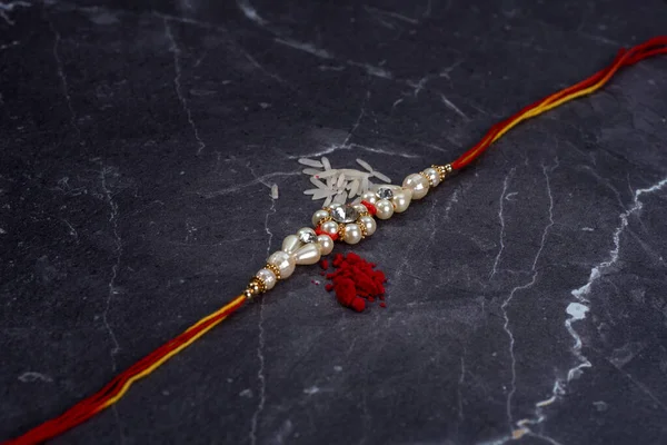 Raksha Bandhan : Rakhi with rice grains and kumkum on stone background, Traditional Indian wrist band which is a symbol of love between Brothers and Sisters. — Stock Photo, Image