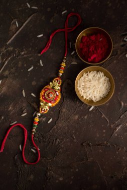 Raksha Bandhan 'ın arkaplanı zarif bir Rakhi, pirinç taneleri ve Kumkum. Geleneksel Hint bilekliği Kardeşler ve Kız Kardeşler arasındaki aşkın sembolüdür..