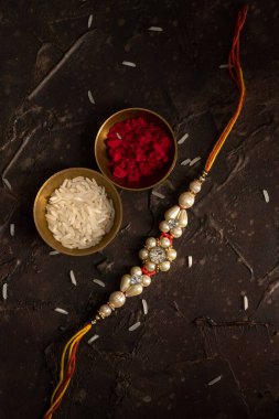 Raksha Bandhan 'ın arkaplanı zarif bir Rakhi, pirinç taneleri ve Kumkum. Geleneksel Hint bilekliği Kardeşler ve Kız Kardeşler arasındaki aşkın sembolüdür..