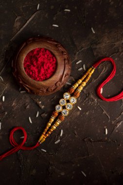 Raksha Bandhan 'ın arkaplanı zarif bir Rakhi, pirinç taneleri ve Kumkum. Geleneksel Hint bilekliği Kardeşler ve Kız Kardeşler arasındaki aşkın sembolüdür..