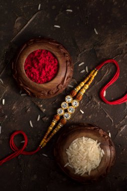 Raksha Bandhan 'ın arkaplanı zarif bir Rakhi, pirinç taneleri ve Kumkum. Geleneksel Hint bilekliği Kardeşler ve Kız Kardeşler arasındaki aşkın sembolüdür..
