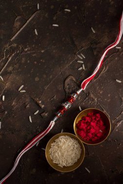 Raksha Bandhan 'ın arkaplanı zarif bir Rakhi, pirinç taneleri ve Kumkum. Geleneksel Hint bilekliği Kardeşler ve Kız Kardeşler arasındaki aşkın sembolüdür..