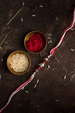 Raksha Bandhan 'ın arkaplanı zarif bir Rakhi, pirinç taneleri ve Kumkum. Geleneksel Hint bilekliği Kardeşler ve Kız Kardeşler arasındaki aşkın sembolüdür..