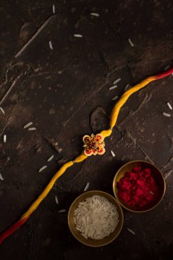 Raksha Bandhan 'ın arkaplanı zarif bir Rakhi, pirinç taneleri ve Kumkum. Geleneksel Hint bilekliği Kardeşler ve Kız Kardeşler arasındaki aşkın sembolüdür..