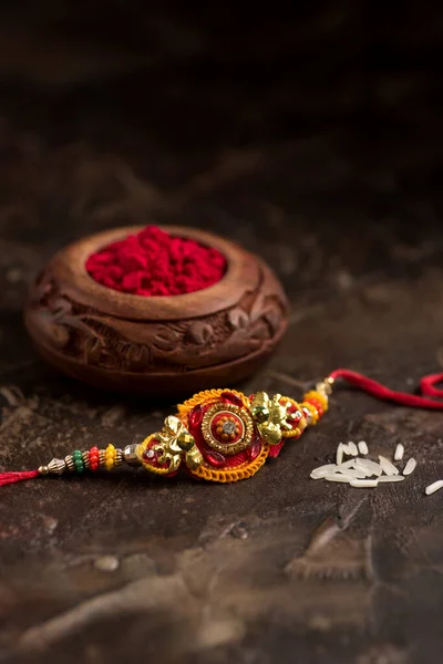 Raksha Bandhan achtergrond met een elegante Rakhi, Rijst Grains en Kumkum. Een traditionele Indiase polsband die symbool staat voor liefde tussen Broeders en Zusters. — Stockfoto