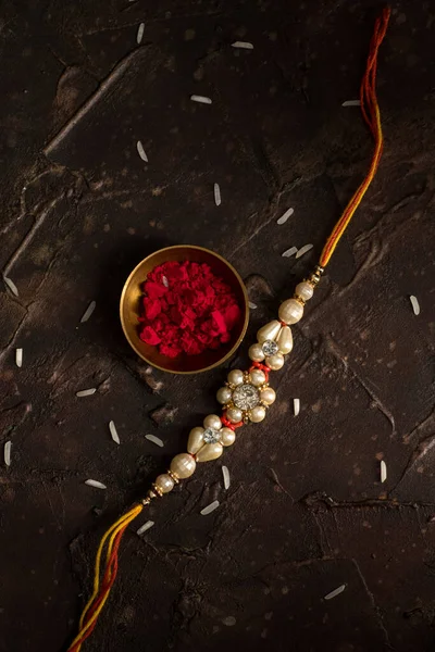 Raksha Bandhan Hintergrund mit einem eleganten Rakhi, Reiskörner und Kumkum. ein traditionelles indisches Armband, das ein Symbol der Liebe zwischen Brüdern und Schwestern ist. — Stockfoto