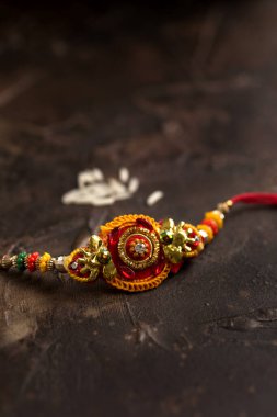 Raksha Bandhan zarif bir Rakhi ve dağınık pirinçle arka planda. Geleneksel Hint bilekliği Kardeşler ve Kız Kardeşler arasındaki aşkın sembolüdür..