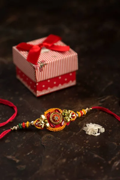 Raksha Bandhan achtergrond met een elegante Rakhi, Rijstkorrels, Kumkum en geschenkdoos. Een traditionele Indiase polsband die symbool staat voor liefde tussen Broeders en Zusters. — Stockfoto