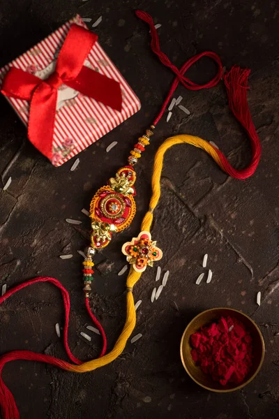 Raksha Bandhan bakgrund med en elegant Rakhi, riskorn, Kumkum och presentförpackning. Ett traditionellt indiskt armband som är en symbol för kärlek mellan bröder och systrar. — Stockfoto