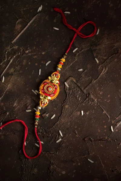 Raksha Bandhan fundal cu un elegant Rakhi și orez împrăștiat. O trupă tradițională indiană de încheietură a mâinii, care este un simbol al iubirii dintre frați și surori . — Fotografie, imagine de stoc