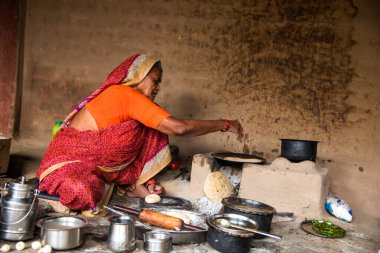 Chikhaldara, Maharashtra - 28 Ağustos 2018: Kimliği belirlenemeyen yaşlı bir kadın, eski bir mutfağın kırsal kesiminde toprak chulhas yakacak odun kullanarak taze yemek yapıyor ve pişiriyor..