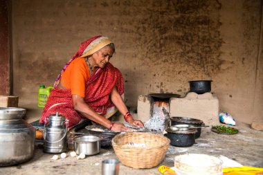 Chikhaldara, Maharashtra - 28 Ağustos 2018: Kimliği belirlenemeyen yaşlı bir kadın, eski bir mutfağın kırsal kesiminde toprak chulhas yakacak odun kullanarak taze yemek yapıyor ve pişiriyor..