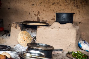Chikhaldara, Maharashtra - 28 Ağustos 2018: Kimliği belirlenemeyen yaşlı bir kadın, eski bir mutfağın kırsal kesiminde toprak chulhas yakacak odun kullanarak taze yemek yapıyor ve pişiriyor..