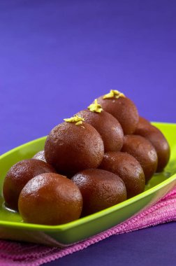 Hint Tatlısı Gulab Jamun 'u tabakta mor arka planda peçeteyle