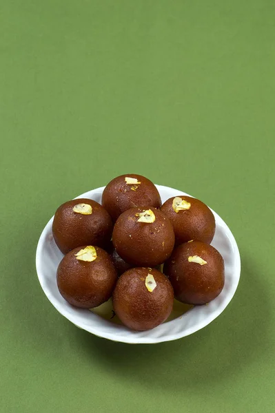 Gulab jamun, indisches Dessert mit Pistazien in weißem Teller auf grünem Hintergrund — Stockfoto