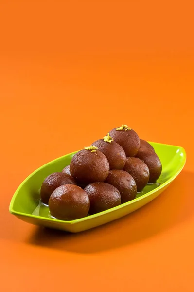 Индийский десерт Гулаб Джамун в тарелке на оранжевом фоне — стоковое фото