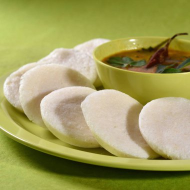 Sambar 'ın yeşil arka planda olduğu Idli, Hint Dili: Güney Hint yemekleri rava idli veya irmik ya da rava tembelce, sambar ve yeşil hindistan cevizi turşusuyla servis edilir..