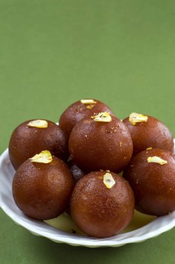 Gulab Jamun, yeşil arka planda beyaz tabakta fıstıklı Hint tatlısı.