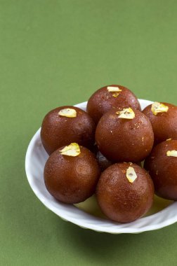 Gulab Jamun, yeşil arka planda beyaz tabakta fıstıklı Hint tatlısı.