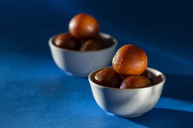 Hint Tatlısı: Gulab Jamun kasede mavi arka planda kaşıkla