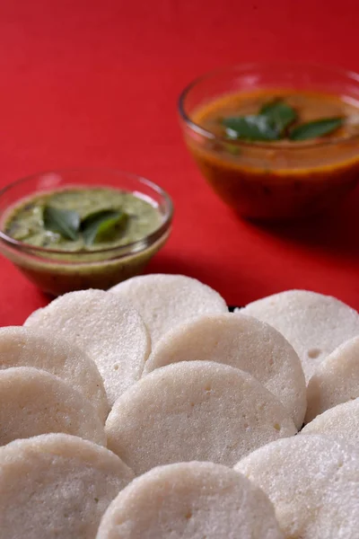 赤の背景にサンバーとココナッツチャツネとイドリ インド料理 南インドのお気に入りの食べ物のラバイドリまたはセモリナまたはラヴァをぼんやりと サンバーと緑のチャツネを添えて — ストック写真